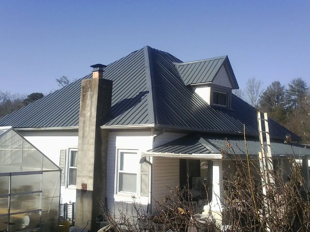 Dark blue standing seam metal roof on a white farmhouse with dormer — Slate & Tile Roof Repair by Roofing Brothers in Dryden