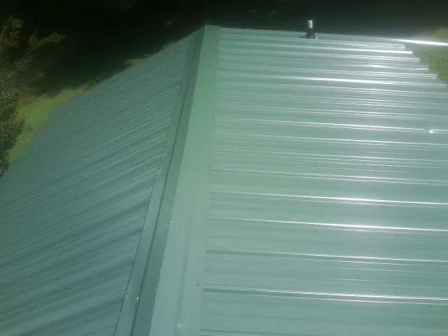 New green metal panels meeting at the ridge of a roof — Flat Roof Repair work by our crew in Dryden