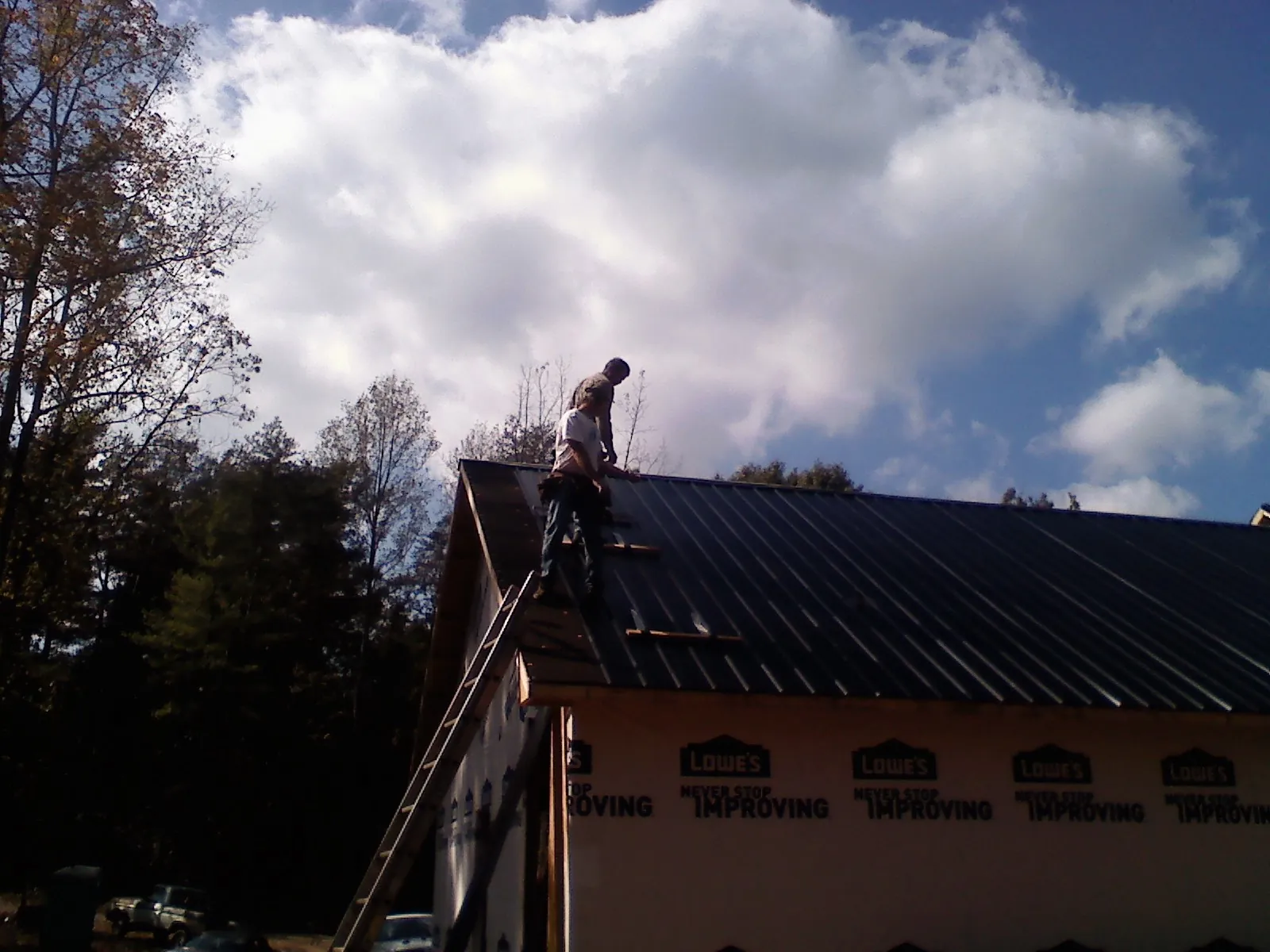 Roofer fastening dark metal panels high against a cloudy sky, from a Roof Inspection job in Dryden