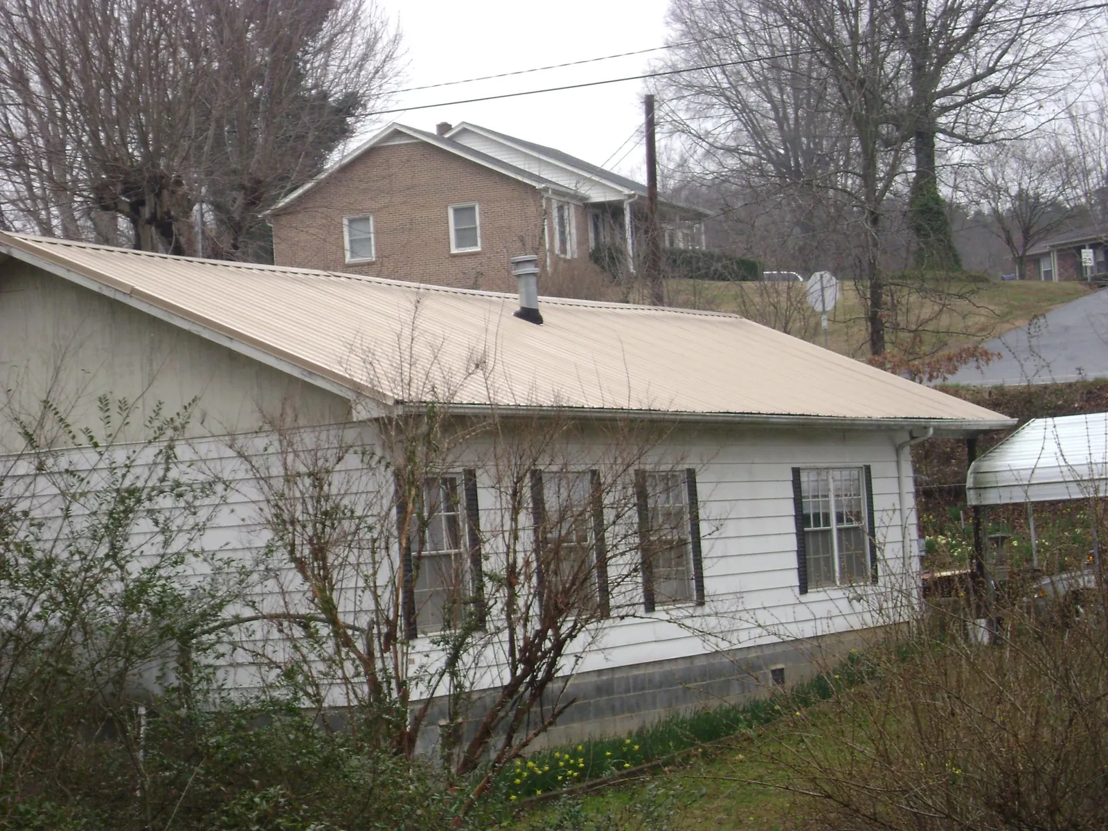 Tan metal roof on a white sided house set into a hillside — Commercial Roofing by Roofing Brothers in Dryden
